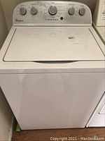 Front view of the white Whirlpool top load washing machine with lid closed, showing control panel with multiple dials and Whirlpool logo.
