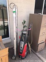 Power washer and hand cart side by side against wall with window and filing cabinet