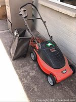 Side view of red and black Black and Decker mower with catch bag and cord, showing full unit from handle to wheels.
