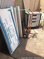 Photo showing multipurpose folding table box, rolls of chicken wire mesh, and two-wheeled hand cart with brown handle in outdoor area
