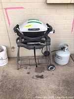 Frontal view of the grill and propane tank showing whole unit and tank beside.