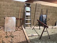 Lot showing the aluminum ladder, wheelbarrow, two saw horses, metal tray, and rake outdoors against a brick wall.