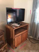 Front view of TV on wooden cabinet in carpeted room showing TV screen and cabinet doors, including carpet area and curtain in background.