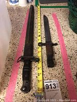 Two edged weapons side by side with measuring tape showing approx 22 inch length