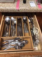 Open drawer showing organized stainless steel flatware including forks, knives, and spoons in a wooden tray.