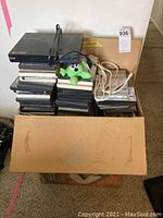 Cardboard box with LG DVD player, piles of DVDs and CDs, extension cord, and plush toy inside.