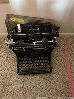 View of the front of the Underwood typewriter with cover draped behind, showing brand and size label.