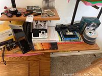 Photo of shelf showing VTech cordless phone, Kodak EasyShare camera in box, magnifying glasses, watches, and office supplies