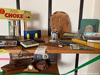 Shelf with various vintage office supplies including stapler, pencil sharpener, protractors, compass, letter opener, and satirical Automotive Choke sign.