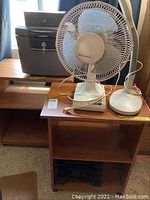 Overview photo showing two wooden shelving units stacked as shelving pieces, Sentry fire safe, tabletop oscillating fan, cash box and fluorescent desk lamp on top of one shelving unit.