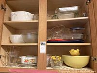 Cabinet filled with various glass and ceramic baking dishes and bowls including vintage Corningware casseroles, Pyrex mixing bowl sets, and clear glass dishes.