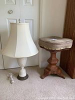 Photo of ceramic lamp with cream pleated shade and vintage wooden stool with worn cushion