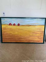 Full view of the framed painting showing a landscape with three red barns in yellow fields under a blue sky.