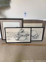 Three framed pencil sketches leaning against a wall on carpet, showing the detailed nature-themed pencil sketches of rocks and foliage. A wooden ruler placed in front marks approximate size.