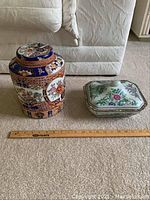 Photo showing two Asian style ceramic decorative containers with a ruler for size reference.