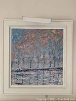 Full view of the framed painting showing the tree line and water with reflection.