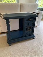 Front view of the dark blue wooden beverage cart showing the drawer and cabinet with brass handles.