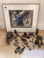 Framed photo of train wheel with assortment of metal miniature figurines in front on floor