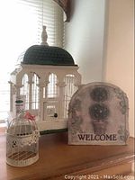 Photo showing full view of bird cage with ceramic tile dome roof and garden welcome sign displaying 'WELCOME'
