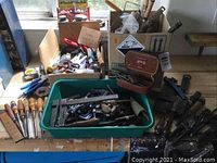 Overview of lot with boxes of assorted hand tools on table, including chisels and clamps
