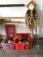 Overview of the lot showing garden scarecrow, storage bins with gardening and car cleaning tools, broom with dustpan leaning against wall and tool rack above.