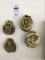 Four horse brass medallions shown from front with embossed detailed designs including a castle and horse head