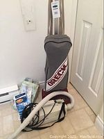 Photo of the Oreck upright vacuum cleaner with gray bag and vacuum accessories including hose, bags, and cords.