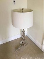 Full view of the 33-inch tall lamp with a silver base and white drum shade against a white wall.