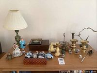 Full lot displayed on wooden table with brass items, figurines, box, and lamp