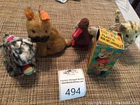Front view of four assorted vintage plush wind-up animal toys including dog, duck, and cats on brown textured surface.