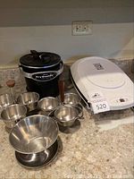 Photo showing Presto FryDaddy deep fryer, set of stainless steel condiment bowls, and George Foreman grill on countertop.