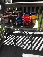 Folding table with ceramic and resin flower pots placed on top, showing size and color variety of pots.