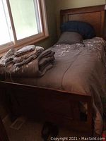 Twin bed fully made with bedding and extra comforter folded on top, showing the headboard and footboard in medium-dark wood finish