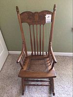 Front view of the wooden rocking chair showing carved details on the top rail and spindle backrest.