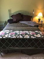 Full view of queen metal bed frame with floral bedding, pillows, and lamp on end table