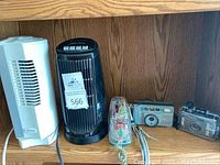 Wide shot showing two small fans, two waterproof cameras and a kitchen timer on a wooden surface, providing an overview of the lot contents.