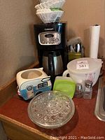 Photo of Cuisinart coffee maker and surrounding kitchen items including camper ceramic dish, glass candy dish, measuring cup, salt and pepper shakers, and silverware holder