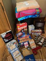 Full view of lot showing games, sleeping bag, and beach towels stacked on floor.