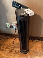 Front angled view showing the digital control panel and overall tower heater unit on wooden floor against wall.