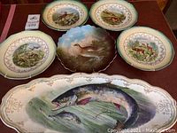 Six decorative plates displayed on table showing variety of animal scenes including deer, fish, rabbits, fox, surrounded by floral borders.