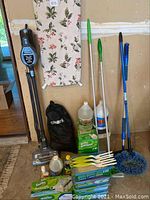 Front view of vacuum, ironing board, cleaning supplies and accessories arranged on floor and wall.