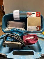Blue Makita electric sander in blue carrying case with cord, sanding sheets, red dust bag, and box of Porter-Cable sandpaper visible.