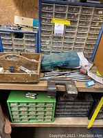 Wooden bench surface with a metal organizer cabinet with multiple drawers on top; green and black plastic drawer units below; wooden tool caddy with miscellaneous tools