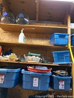 Multiple blue plastic storage bins on shelves containing a variety of tools and hardware including electrical parts, battery chargers, and miscellaneous items.