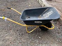 Side view of Jeep wheelbarrow showing black tub and yellow handles on gravel surface