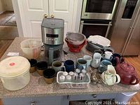 Photo of the entire lot showing coffee makers, mugs, colanders, pitchers, measuring cups, bakeware, and plastic containers