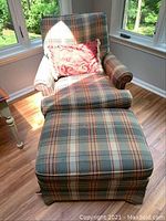 Plaid swivel armchair with ottoman and red decorative pillow in window alcove, showing the color and pattern of the fabric.