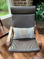 Full view of IKEA leather armchair with wooden arms and brown leather cushions, includes decorative lumbar pillow.