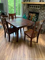 Photo of full vintage dining set showing square wooden table with four matching chairs around it on a wood floor.