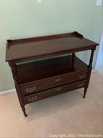 Front view of dark wooden sideboard with two drawers, open middle shelf, turned legs, and caster wheels.
